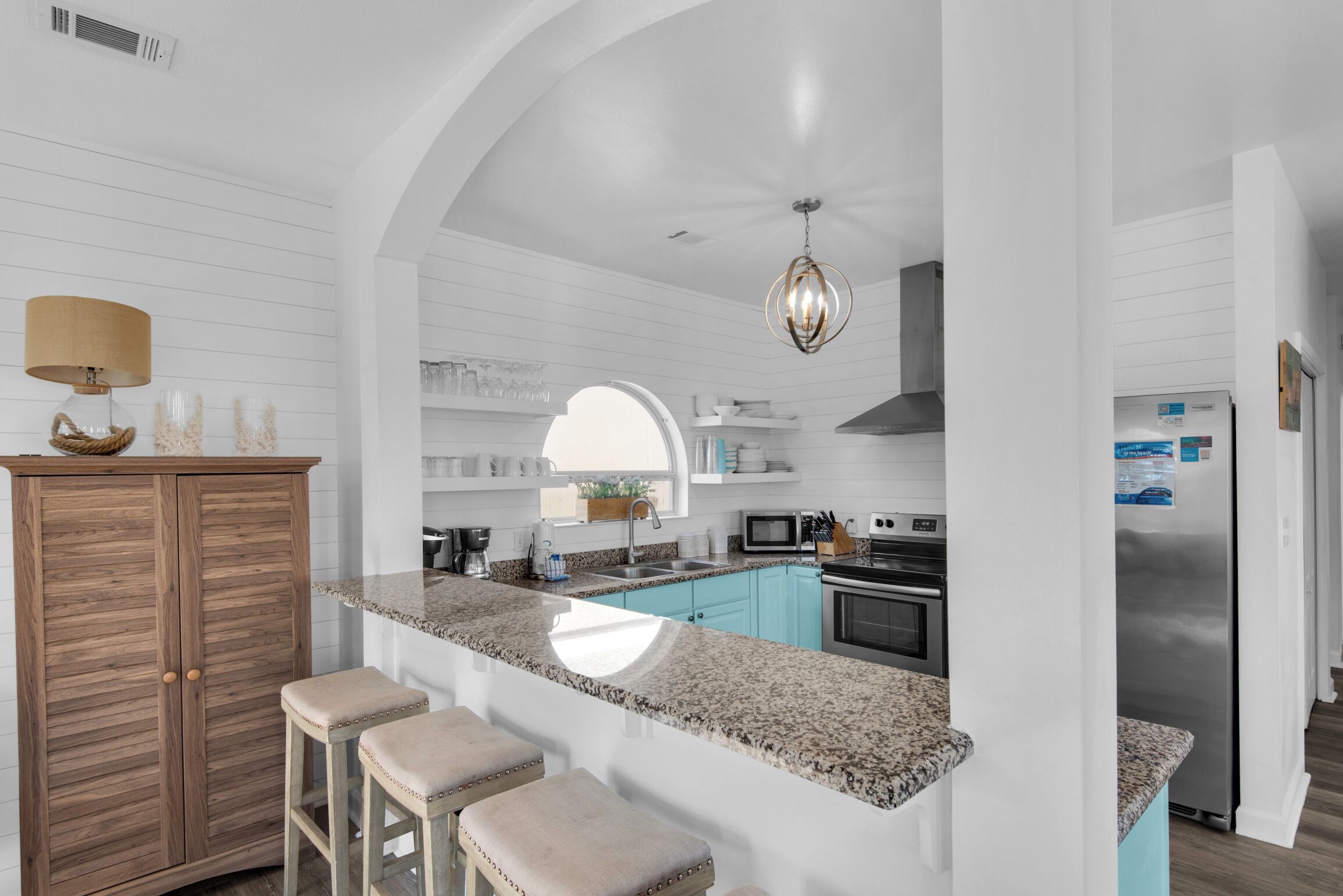 A modern kitchen with a granite countertop, wooden cabinets, and a built-in island with bar stools.
