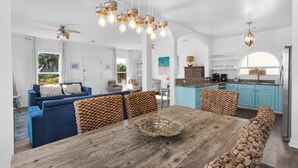 A spacious living area with a wooden dining table, blue sofas, and patterned cushions.