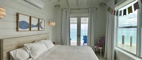 A bedroom with a large bed, a view of the sea through a glass door, and a ceiling fan.