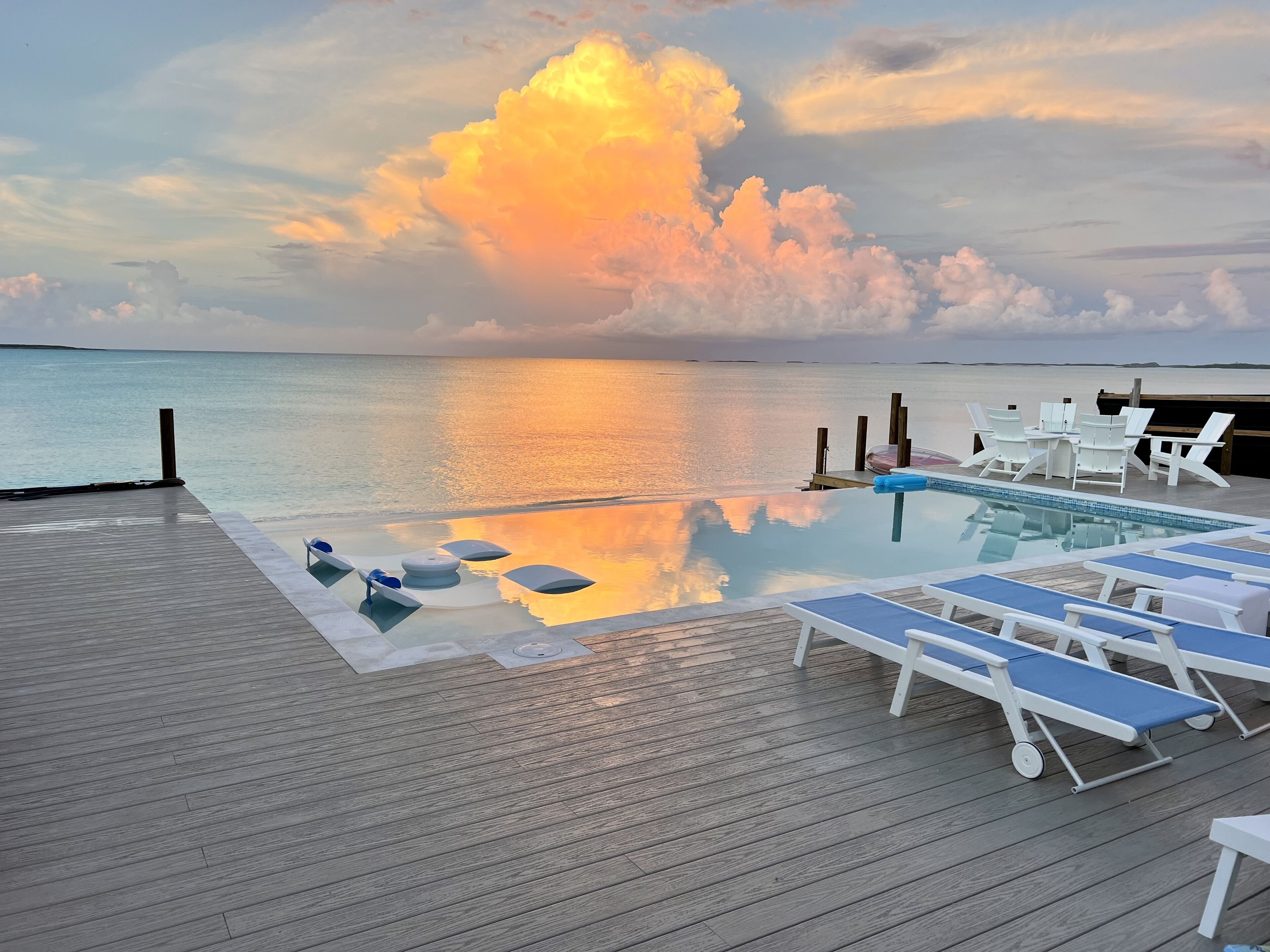 Una piscina infinita con sillas de descanso y una terraza de madera con vistas al mar.