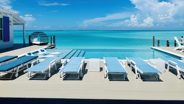A poolside area with lounge chairs and a cabana overlooking a clear blue sea. - Luxury beachfront home, Heated private pool, Five King suites w/ ensuite baths! (Georgetown)