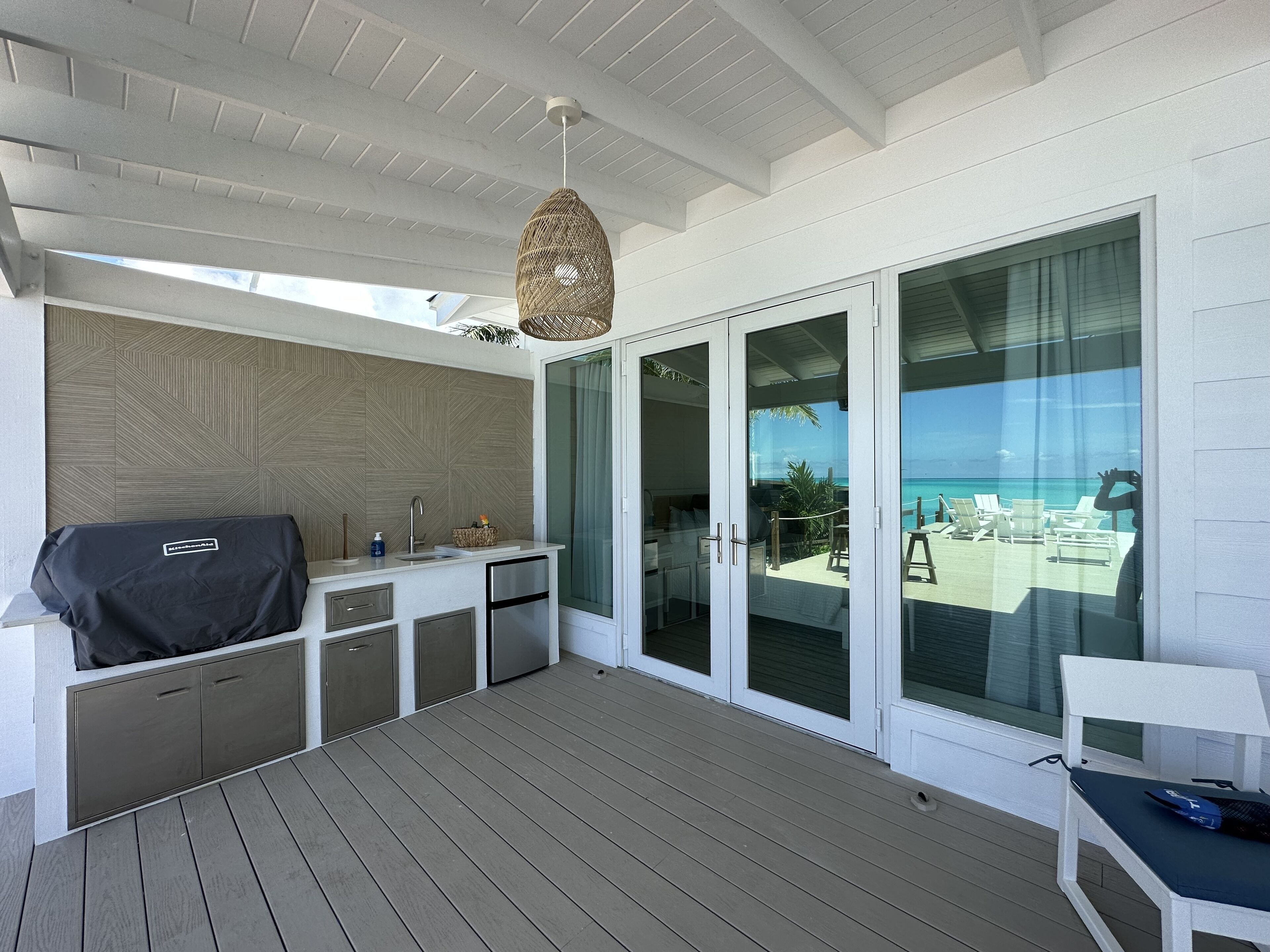 A covered outdoor area with a grill, a sink, and a seating area with a view of the ocean.
