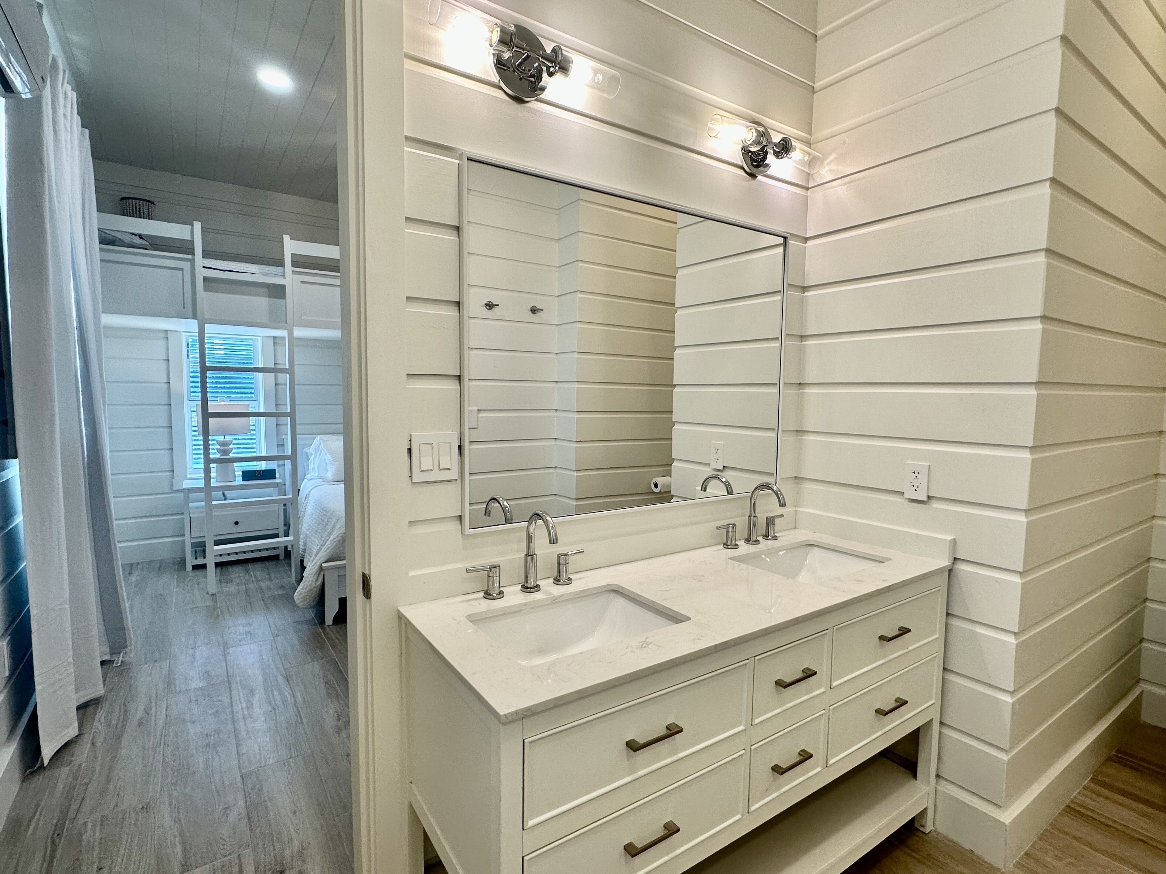 A modern bathroom with a large mirror, two sinks, and a walk-in closet.