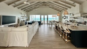 A spacious living area with a large TV, a sofa, and a dining area with a view of the ocean. - Luxury beachfront home, Heated private pool, Five King suites w/ ensuite baths! (Georgetown)