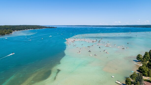 Vue aérienne d’une zone côtière avec des eaux cristallines, des bateaux et une plage de sable.