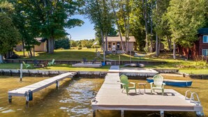 Une jetée avec des chaises et un petit bateau, entourée d’arbres et avec une maison en arrière-plan.