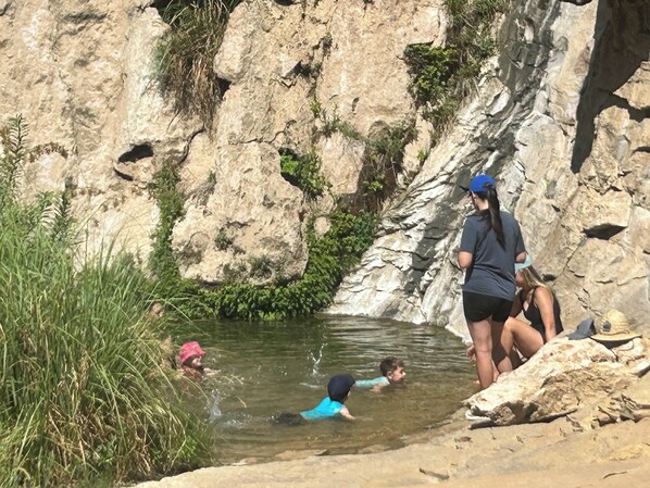 A rocky landscape with a shallow water body, vegetation, and people engaging in water activities.