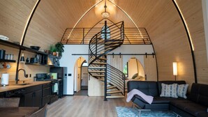 Ein modernes Interieur mit Holzboden, einer Wendeltreppe, einer Küchenzeile und einer Sitzecke inklusive Sofa und Couchtisch.