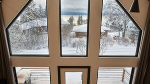 Tunnelmallinen sisustus, jossa on suuri ikkuna, josta avautuu lumipeitteinen maisema, puinen ruokailutila ja tummanvärinen sohva.