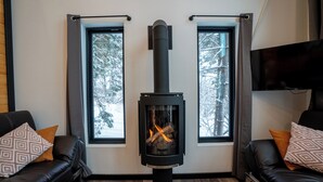 Moderni olohuone, jossa on musta puukamiina, kaksi mustaa nahkasohvaa, kuviollisia koristetyynyjä ja seinälle asennettu litteä televisio.