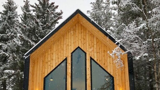 Puinen mökki, jossa on keskeinen sisäänkäynti, suuret ikkunat ja portaat, jotka johtavat terassille.