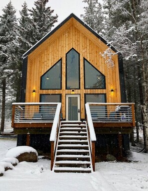 Une cabane en bois avec une entrée centrale, de grandes fenêtres et un escalier menant à une terrasse.