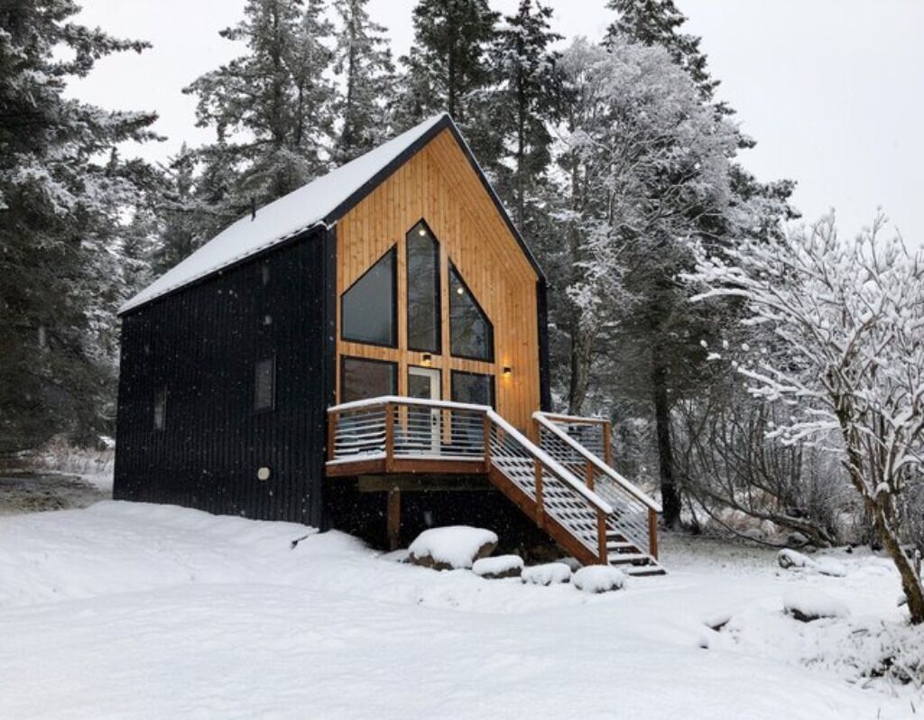 Eine Holzhütte mit einem steilen Dach, großen Fenstern und einer Holztreppe zu einer Terrasse.