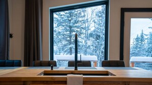 Ein moderner Essbereich mit einem Holztisch, schwarzen Stühlen und einem großen Fenster mit Blick auf einen verschneiten Wald.