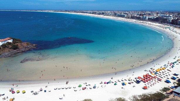 A coastal cityscape with a wide beach, clear blue waters, and a dense urban area in the background. - Cabo Frio Parque Burle Aluguel Economico (Cabo Frio)