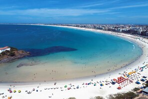 A coastal cityscape with a wide beach, clear blue waters, and a dense urban area in the background. - Cabo Frio Parque Burle Aluguel Economico (Cabo Frio)