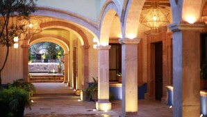 Un pasillo exterior cubierto con arcos, columnas e iluminación colgante.