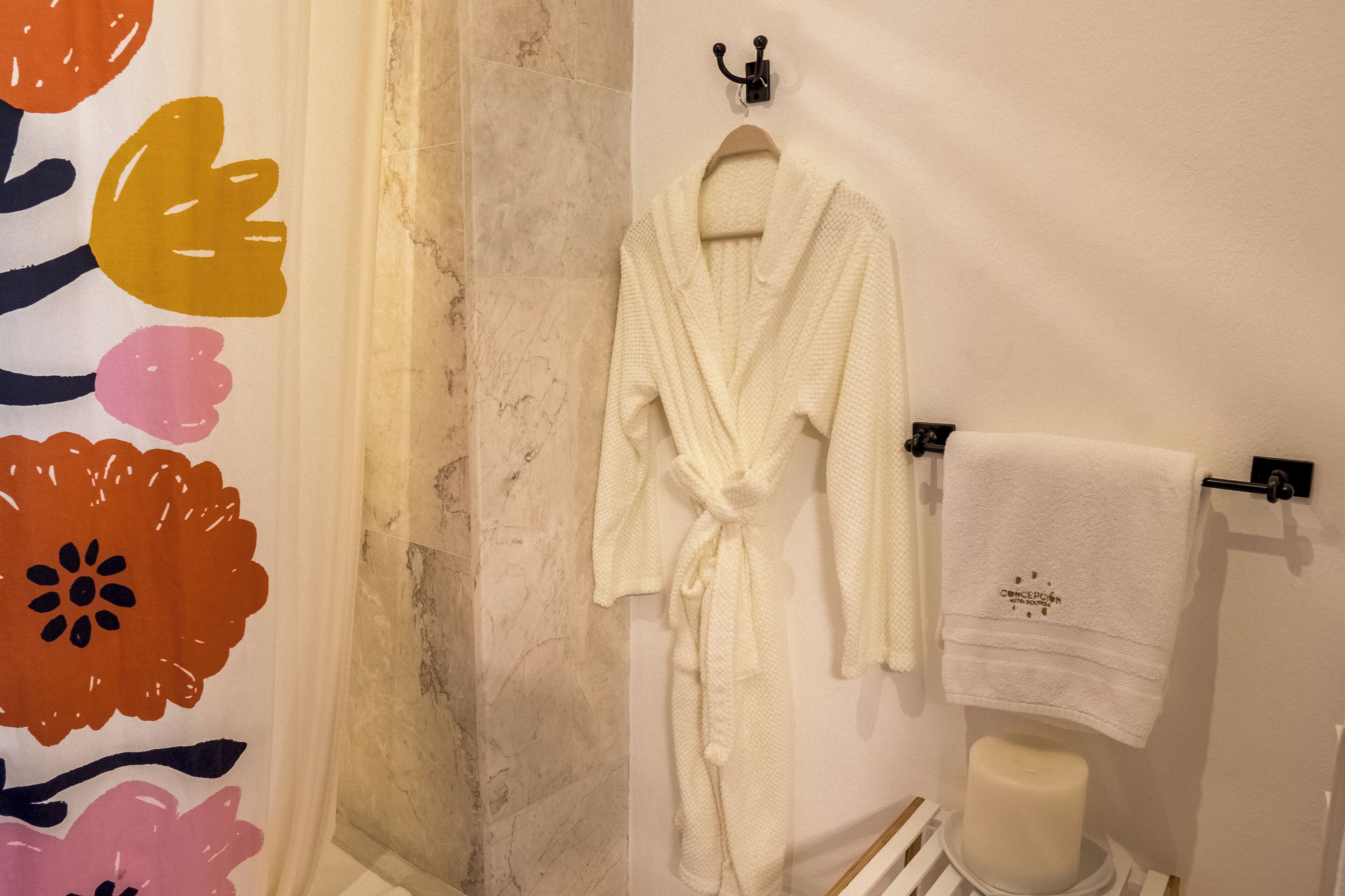 A bathroom with a white bathrobe hanging on a hook, a white towel on a towel rack, and a toilet with a white tissue box.