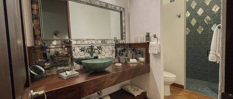 A bathroom with a large mirror, a bowl sink, a toilet, and a shower area.