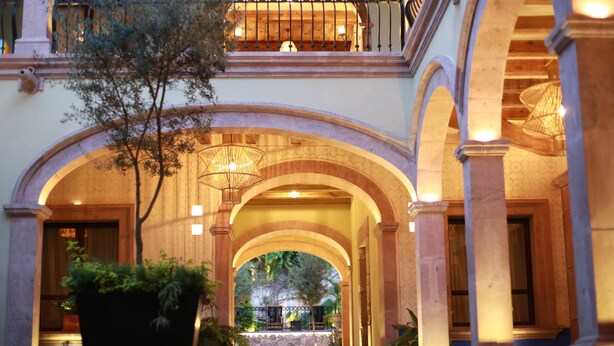 Un majestuoso acceso con columnas arqueadas, una escalera y un balcón con barandillas de hierro forjado.