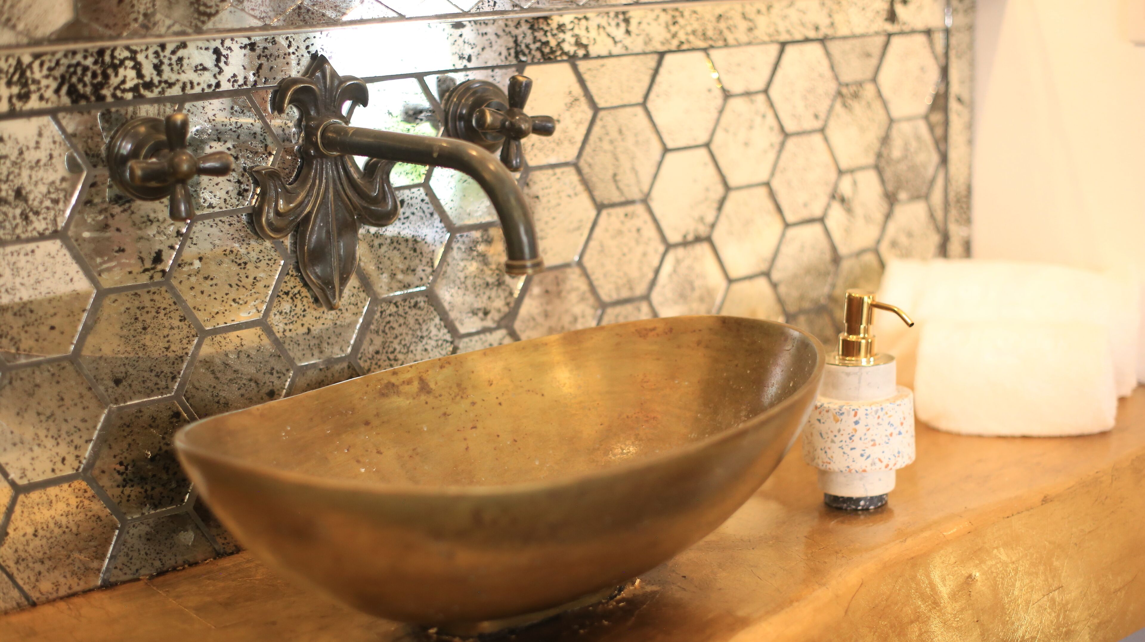 Un baño con salpicadero de azulejos hexagonales, un grifo de latón y un lavabo de latón.