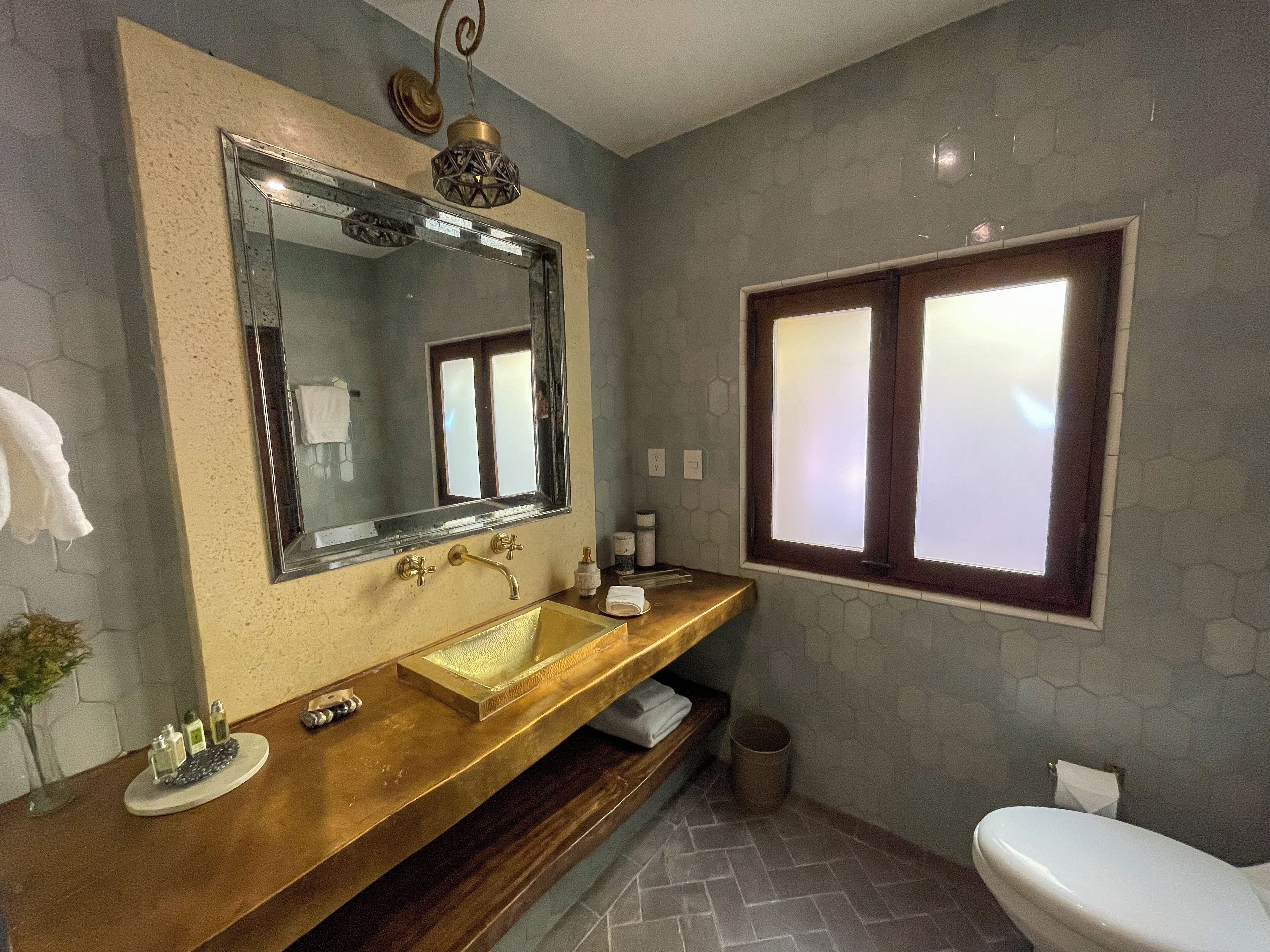 Un baño con un espejo grande, un tocador de madera, un lavabo, un inodoro y una ventana con vidrio esmerilado.