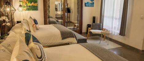 A hotel room with two beds, a small table, a chair, a mirror, and artwork on the walls.