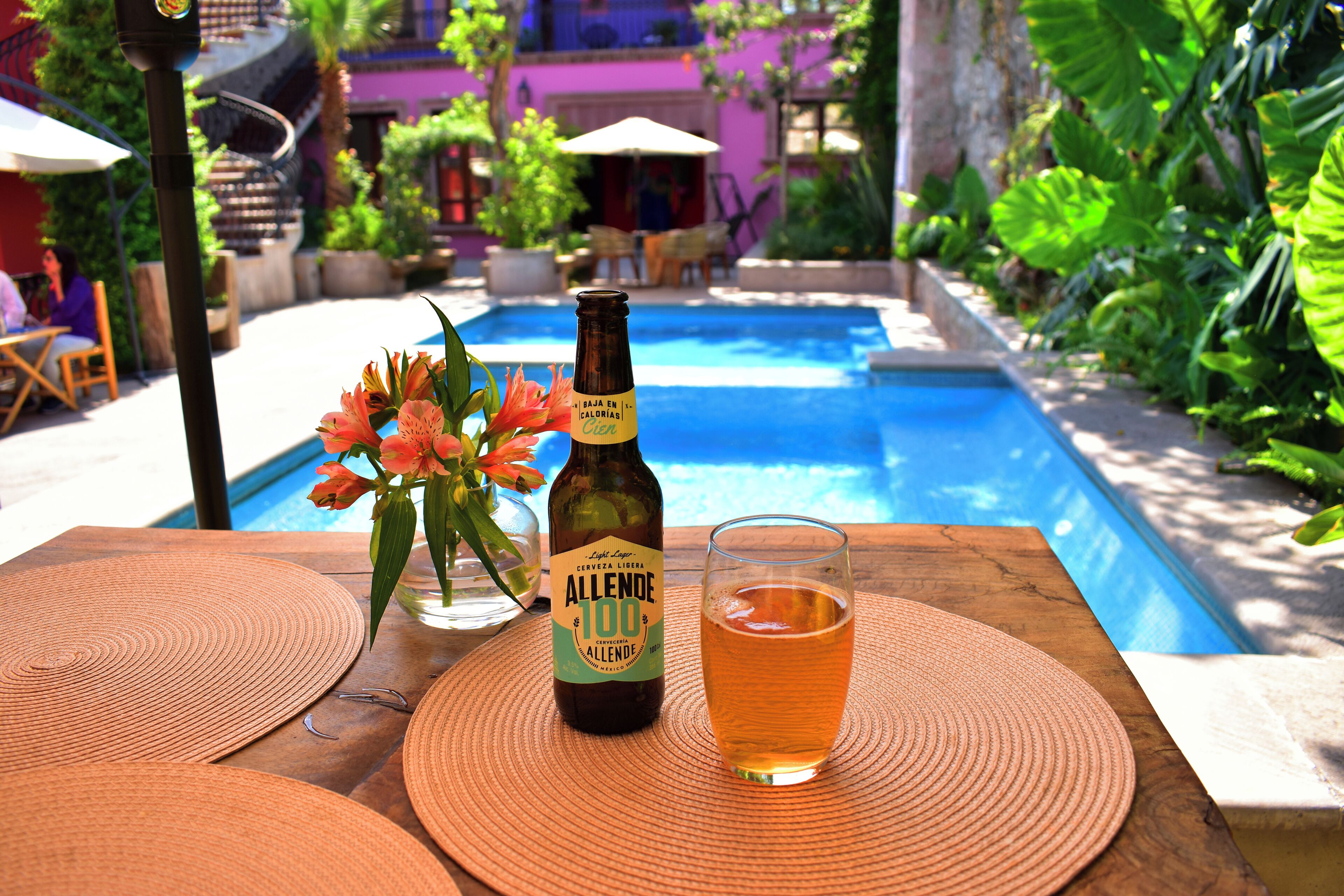 Eine Flasche Bier und ein Glas auf einem Tisch, im Hintergrund ein Pool.