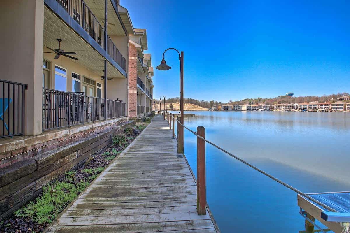 A wooden boardwalk leading to a building with balconies, a calm lake, and a clear sky.
