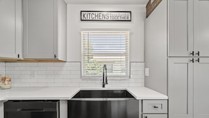 Een keuken met witte kastjes, een roestvrijstalen spoelbak en een raam met jaloezieën.
