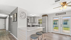 Een moderne keuken met een centraal kookeiland, barkrukken, een klok en een bord met een richting naar het strand.