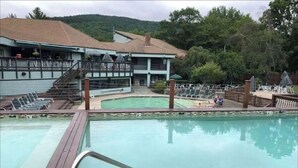 A swimming pool with wooden deck and lounge chairs, surrounded by a building with a balcony and a view of the hills. - My Mountainside Mansion in Waterville Estates!🏔☀️🏊‍♀️⛷ (Campton)