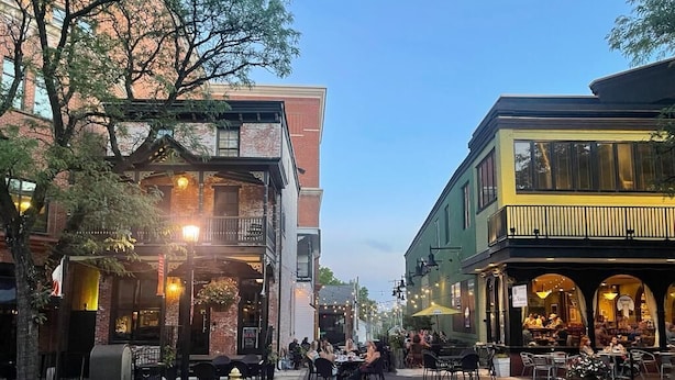 Une rue bordée de cafés avec des terrasses, de bâtiments en briques et un ciel dégagé.