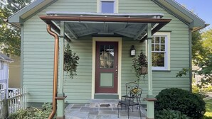 Une maison à deux étages avec un porche à l’avant, une porte rouge et une petite fenêtre au-dessus de la porte.