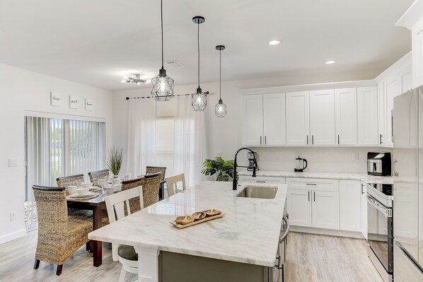 A modern kitchen with white cabinetry, a marble island, and pendant lighting.