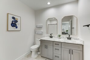 A modern bathroom with a white toilet, a double sink vanity with a marble countertop, and a large mirror above the vanity.