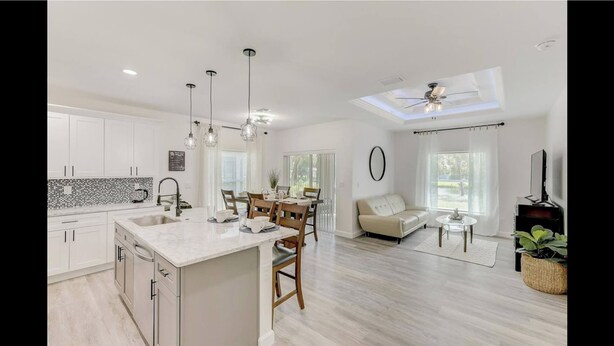 A modern kitchen with white cabinets, a marble island, pendant lighting, and a dining area with a sofa and table. - WaterFront Boundary vacation! Close to beaches 3bdr2bath,golfing fishing (Rotonda West)