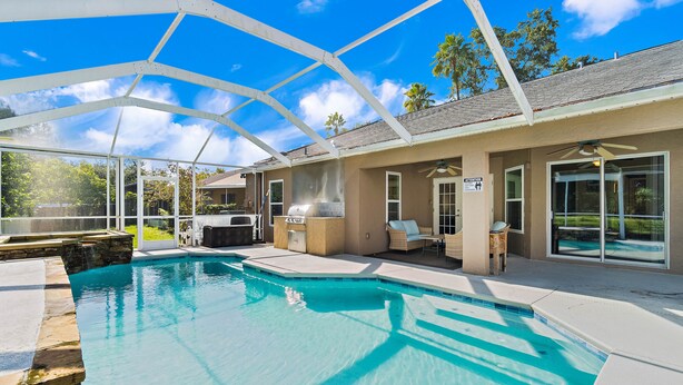 A covered outdoor swimming pool with a barbecue area and lounge chairs.