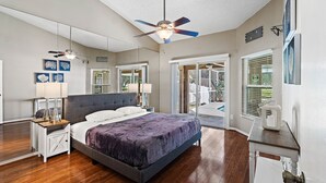 A bedroom with a bed, bedside tables, a ceiling fan, and a view of the outdoors.