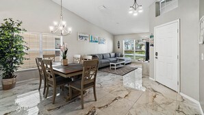 A spacious living area with a dining table, chairs, a sofa, and a chandelier.