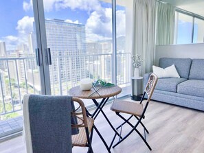 A modern living room with a large balcony, a grey sofa, wicker chairs, and a small round table with a white object on it.