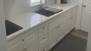 A modern kitchen with white cabinets, a stainless steel sink, a coffee maker, and a built-in microwave. - Remodeled Stand alone Cottage.B (Phoenix)