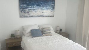 A bedroom with a bed, a nightstand, a lamp, a small potted plant, and a painting on the wall. - Remodeled Stand alone Cottage.B (Phoenix)