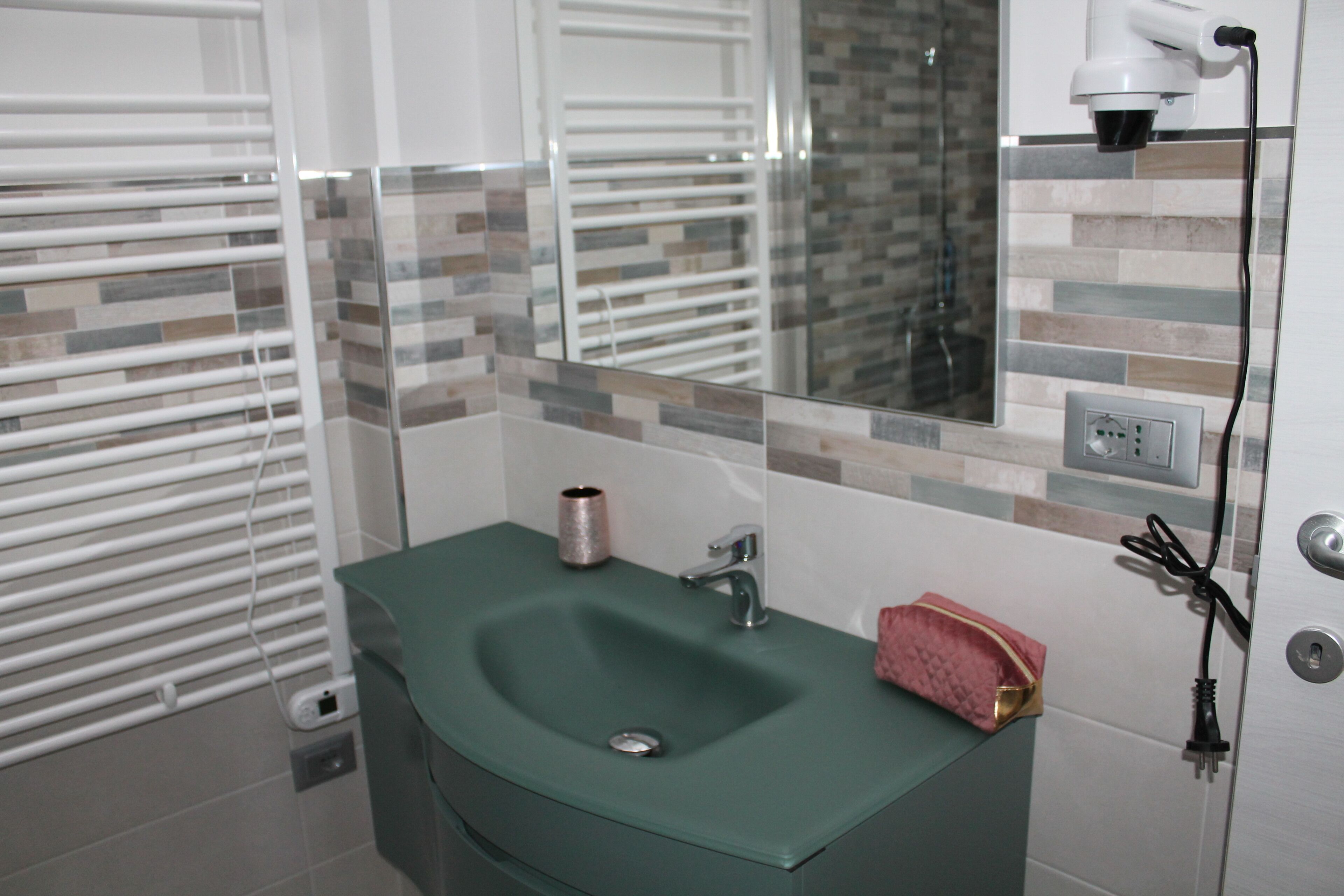 Un bagno con un lavandino verde, uno specchio, un asciugamano e una presa di corrente.