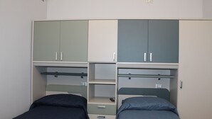 Ein Schlafzimmer mit zwei Einzelbetten, einem Kleiderschrank mit vielen Fächern und einem Regal.