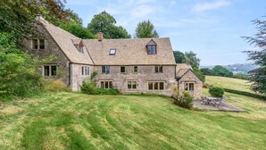 A stone house with multiple windows and a sloped roof, surrounded by a well-maintained lawn and trees.