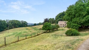 A rural landscape with a stone house surrounded by trees and a fenced field.