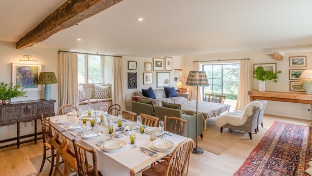 A spacious living area with a dining table set for six, a sofa, and a small seating area with a lamp.