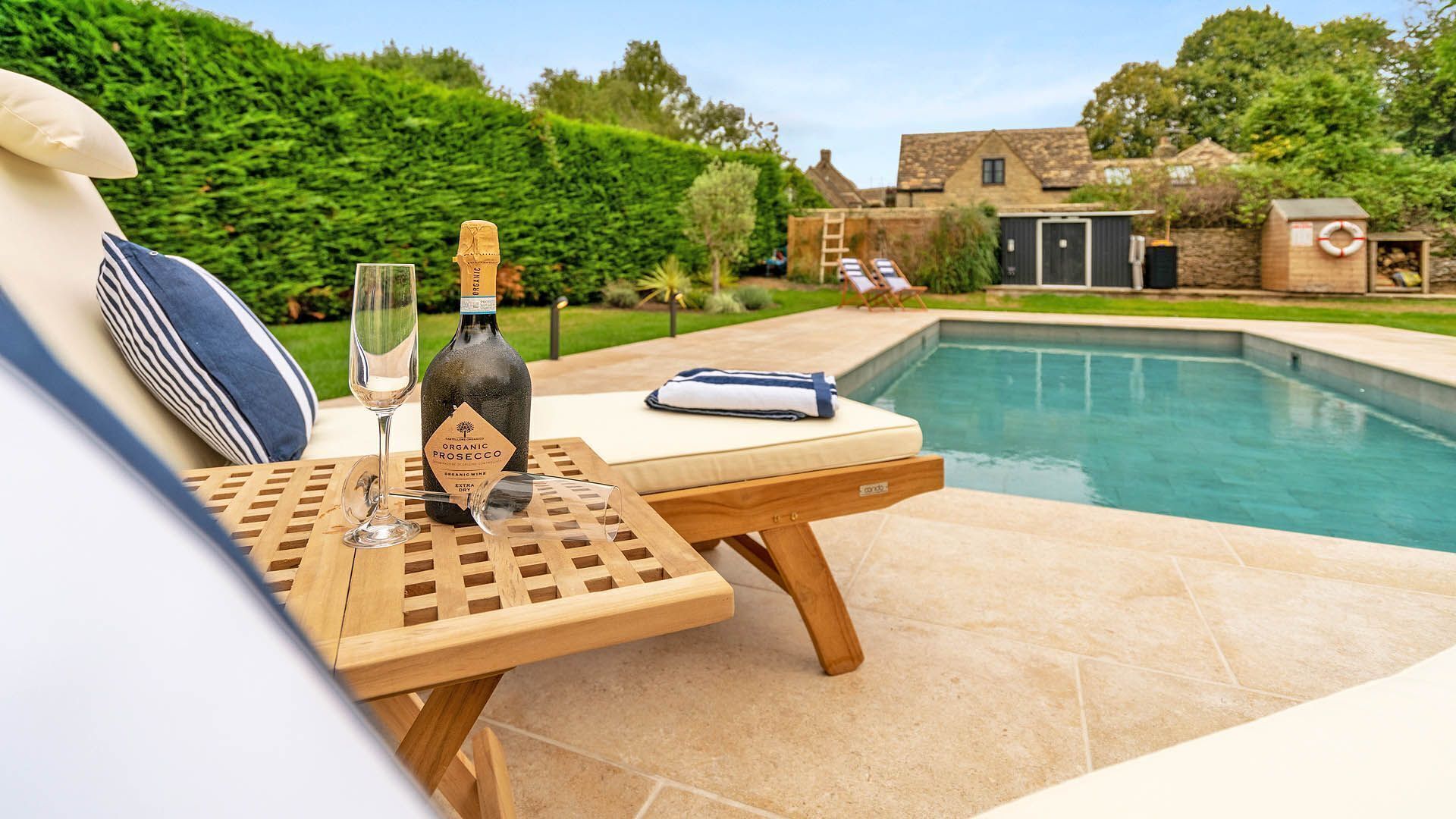 A poolside setting with a table, a bottle of wine, and a glass.