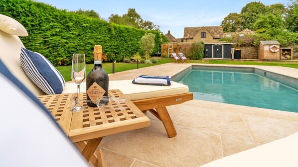A poolside setting with a table, a bottle of wine, and a glass.